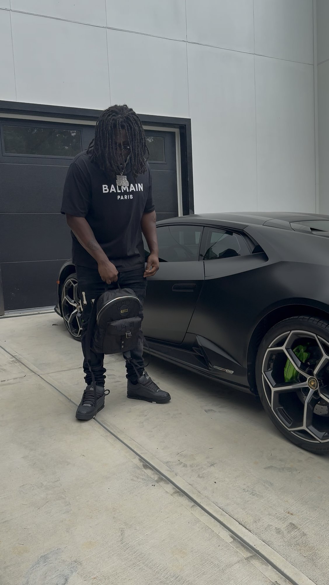 Freeband standing next to a matte black car in front of a garage